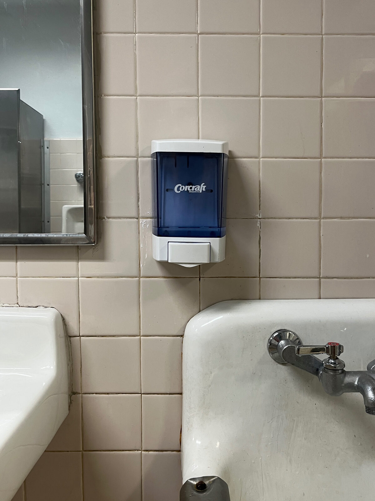 A wall-mounted bulk soap dispenser beside a commercial sink and faucet.